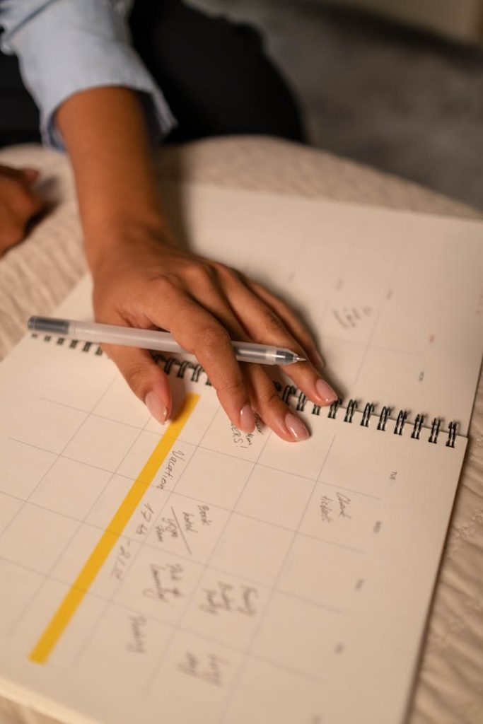 pexels-photo-6862837 A close-up shot of a hand writing in a planner while resting on a bed.